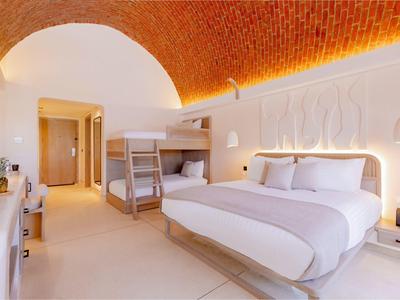 Helles Hotelzimmer mit Doppelbett, Etagenbett und sichtbarer roter Kuppeldecke aus Ziegeln.