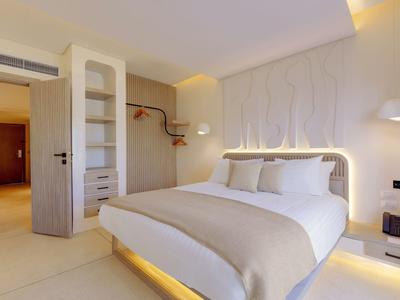 Modernes Schlafzimmer mit großem Bett, eingebautem Regal, warmem Licht und hellem Farbkonzept.
