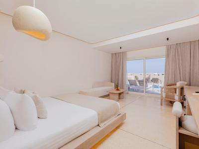 Helles, modernes Hotelzimmer mit Doppelbett, Schreibtisch, Sessel und großem Fenster mit Balkon.