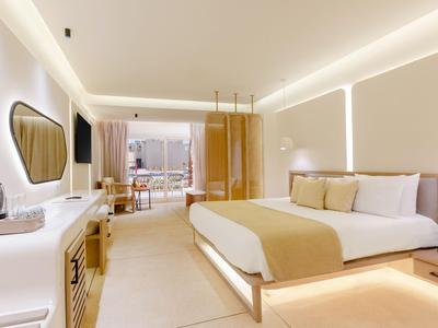 Modernes Hotelzimmer mit großem Bett, warmen Farben und Stadtblick durch die Fenster.