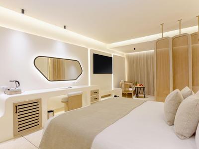 Modernes Hotelzimmer mit großem Bett, flachem Fernseher, Spiegel und heller, minimalistischer Einrichtung.