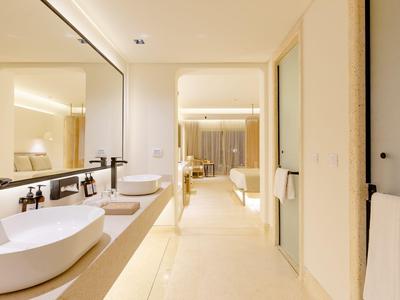 Helles Badezimmer mit Doppelwaschbecken und Blick in ein modernes Schlafzimmer.