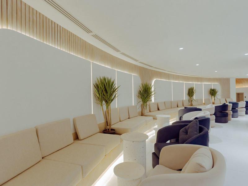 Nowoczesna lobby hotelowa z zakrzywionymi beżowymi sofami, niebieskimi fotelami i roślinami.