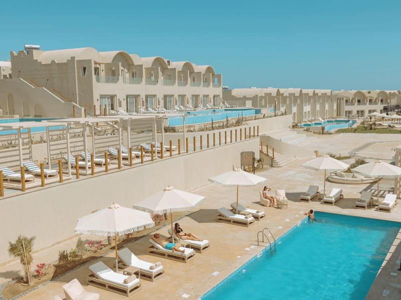 Zewnętrzny basen hotelowy z leżakami i parasolami pod jasnym niebieskim niebem.