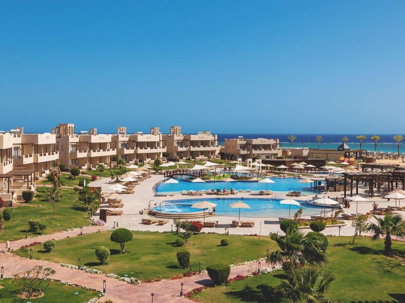 Hotelanlage mit Schwimmbädern, Liegestühlen und gepflegtem Garten unter blauem Himmel am Meer.