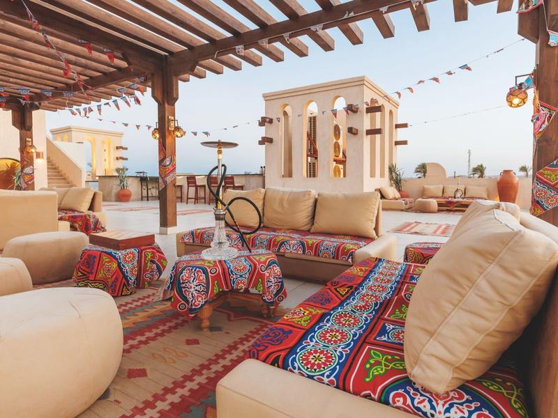 Gemütliche Dachterrasse mit bunten Teppichen, bequemen Sofas und Laternen bei Tageslicht.