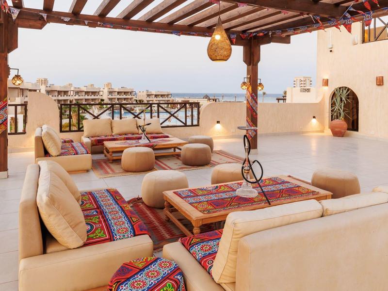 Terrassenlounge mit beigen Sofas, bunten Kissen und Holzbalken, Blick auf Stadt und Himmel.