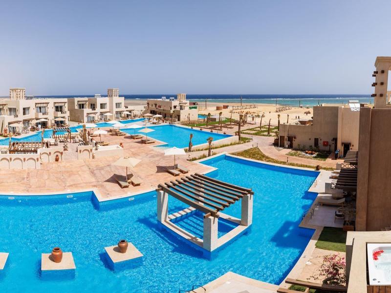 Großer Außenpool mit Liegen, Pergola und Blick auf Meer und sonnigen Himmel.