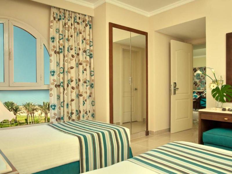 Jasny pokój hotelowy z dwoma łóżkami, widokiem na morze i ciepłą beżową dekoracją.