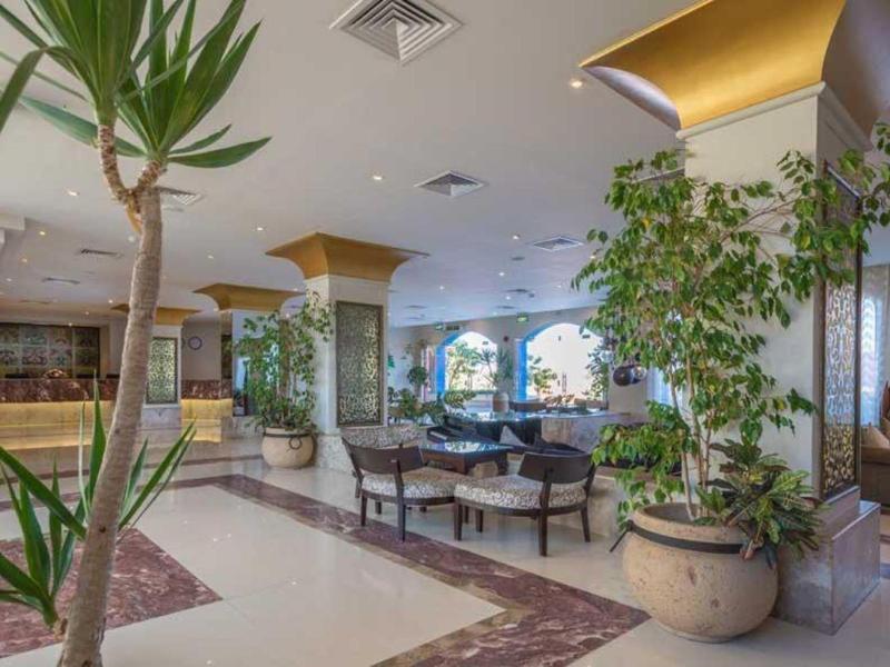 Przestronny hol hotelowy z roślinami, złotymi kolumnami i wygodną częścią wypoczynkową.