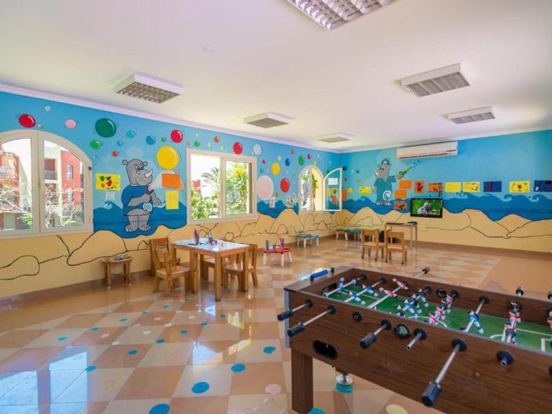 Kolorowa sala zabaw dla dzieci z piłkarzykami i drewnianymi stolikami.