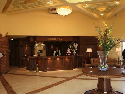 Heller Empfangsbereich mit dunklem Holztresen, Teppichmuster auf Boden und großem Blumenarrangement.