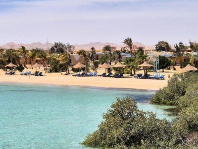 Klarer Strand mit türkisfarbenem Wasser, Palmen und Hotelgebäuden im Hintergrund.