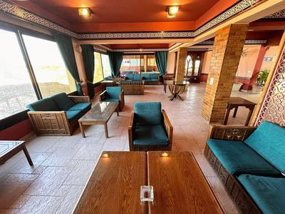 Großer Hotel-Loungebereich mit Holztischen, grünen Sesseln und großen Fenstern mit Aussicht.