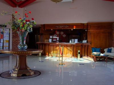 Heller Hotellobby-Empfangsbereich mit Holzmöbeln und Blumenschmuck auf einem runden Tisch.