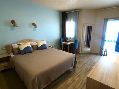 Hell eingerichtetes Hotelzimmer mit großem Bett, Schreibtisch und Balkon.