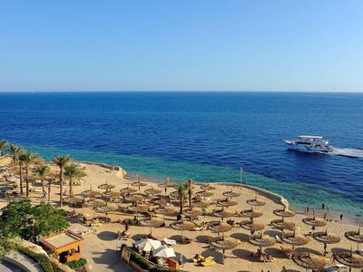 Strand mit Sonnenschirmen, Palmen und einem Boot auf dem ruhigen blauen Meer.