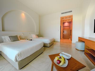 Schlicht eingerichtetes Hotelzimmer mit zwei Betten, Fernseher und Obst auf einem Tisch.