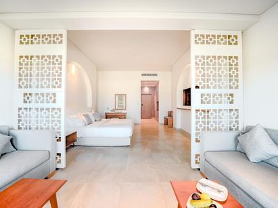 Helles Hotelzimmer mit zwei grauen Sofas, Doppelbett und weißen dekorativen Trennwänden.