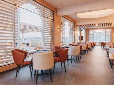 Modernes Hotelrestaurant mit großen Fenstern, bequemen Sesseln und hellem Ambiente.