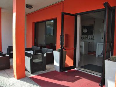 Außenbereich mit orangener Fassade, schwarzem Sitzmöbeln und offener Glastür zum Innenraum.