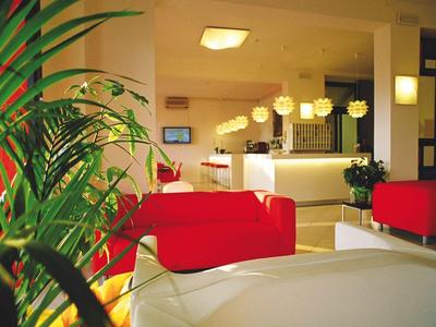 Moderne Hotellobby mit roten Sesseln, Pflanzen und hellem Empfangsbereich.