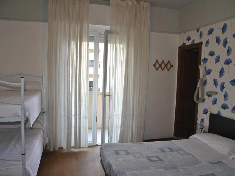 Camera d'hotel con letto a castello, letto matrimoniale, tende chiare e parete decorata