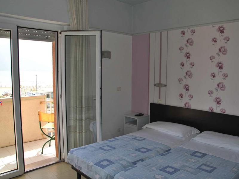 Camera da letto con letto matrimoniale, porta scorrevole in vetro e balcone con vista esterna.