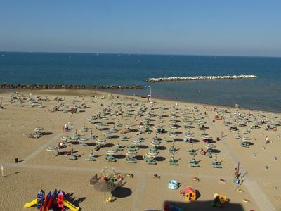 Strand mit zahlreichen Sonnenschirmen, Liegen und ruhigem Meer unter blauem Himmel.
