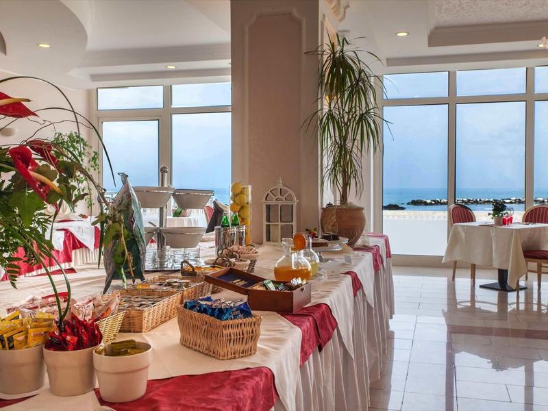 Heller Frühstücksraum mit Buffet, Pflanzen und großem Panoramafenster zum Meer.