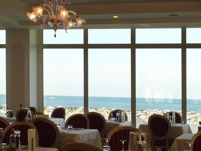 Restaurant mit großen Fenstern, durch die man den Strand und das Meer sieht, helle Atmosphäre.