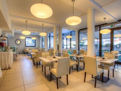 Modernes Restaurant mit hellen Stühlen und Tischen, großen Fenstern und runden Deckenlampen.