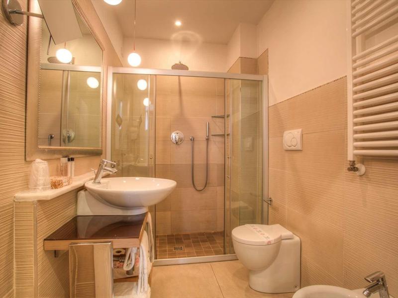 Modernes Badezimmer mit Glas-Dusche, Waschbecken, Toilette, Spiegel und Handtuchheizkörper, beige Fliesen.