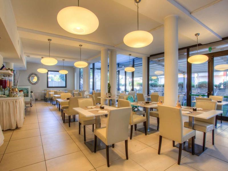 Modernes, helles Restaurant mit beigen Stühlen, Holztischen und großen Fenstern zur Straßenseite.