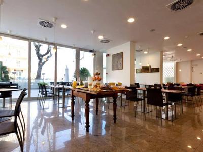 Heller Frühstücksraum mit Tischen, Stühlen und Buffettisch vor großen Fenstern.