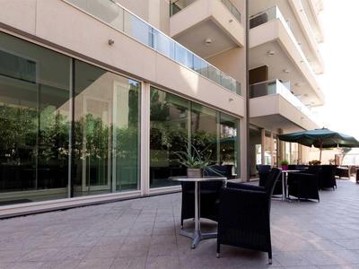 Moderne Außenterrasse mit Glaswänden, schwarzen Stühlen und Tischen unter Sonnenschirmen.