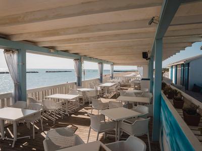 Covered terrace with white tables and chairs by the water overlooking the sea.