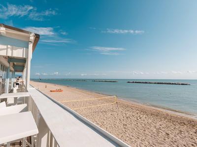 Blick von einer Terrasse auf einen Sandstrand und das Meer unter klarem Himmel.