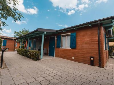 A modern wooden holiday house with blue shutters and a paved front area under a blue sky.