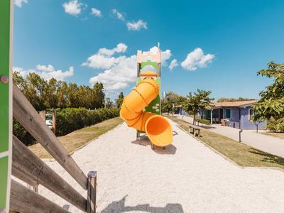 Large orange water slide in a sunny water park next to a blue building.