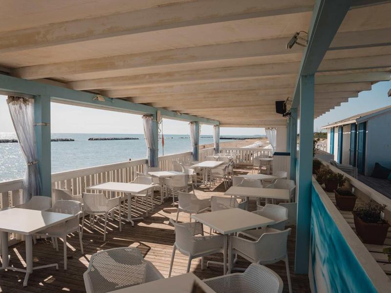 Covered terrace with white tables and chairs by the water overlooking the sea.