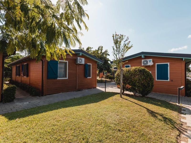 Two red bungalows with air conditioners and walkways in a green area under sunny sky.
