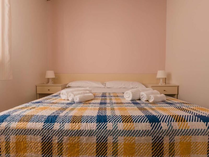 A double bed with a plaid bedspread and two bedside tables in a bright, minimalist room.