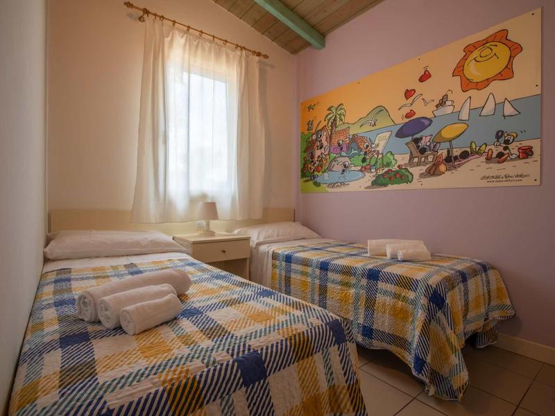 Small bedroom with two single beds, window, colorful wall art, and towels on the beds.