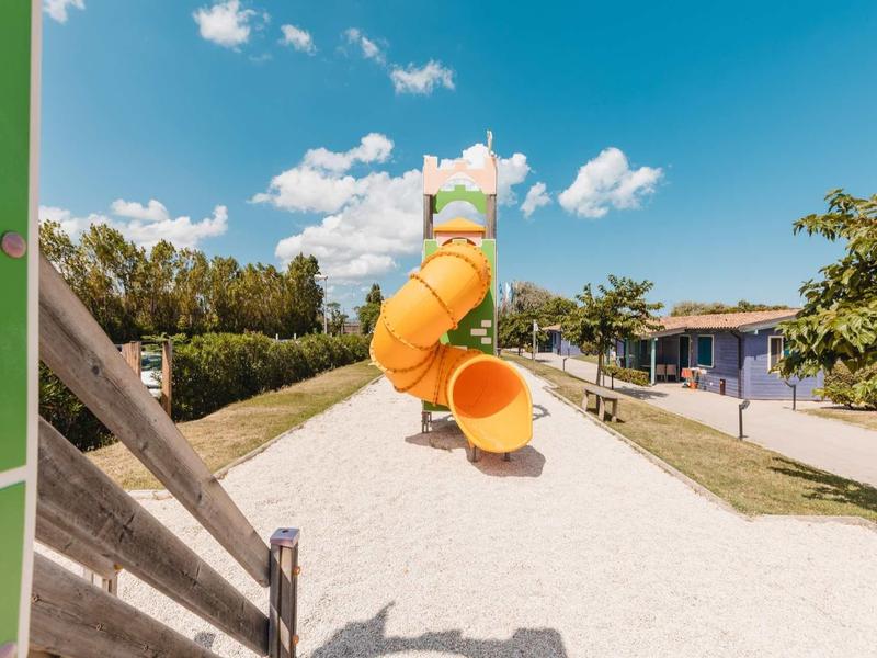 Large orange water slide in a sunny water park next to a blue building.