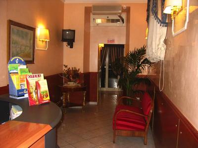 Ein schmaler Raum mit roten Sesseln, Wandlampen, Pflanzen und einem Tisch mit Broschüren.