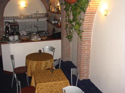 Gemütliches Café mit kleinen runden Tischen und Stühlen neben gemauertem Tresen und Blumenampel.