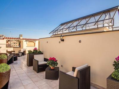 Dachterrasse mit grauen Sitzmöbeln, Pflanzen in Töpfen und Glasdachstruktur bei klarem Himmel.