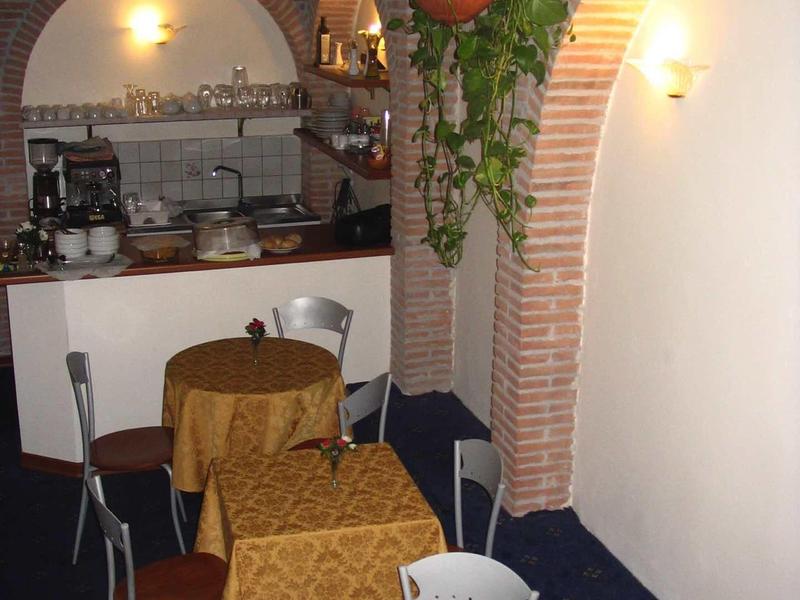 Gemütlicher Gastraum mit braunen Tischen, gemütlichen Stühlen und hängender Pflanze an Backsteinbogen.