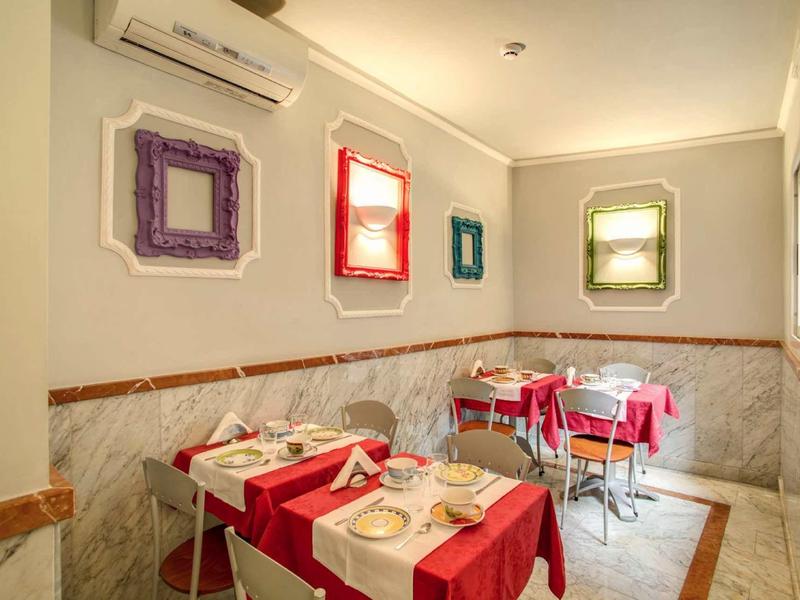 Hell beleuchteter Raum mit roten Tischtüchern, bunten Bilderrahmen und sechs Stühlen.